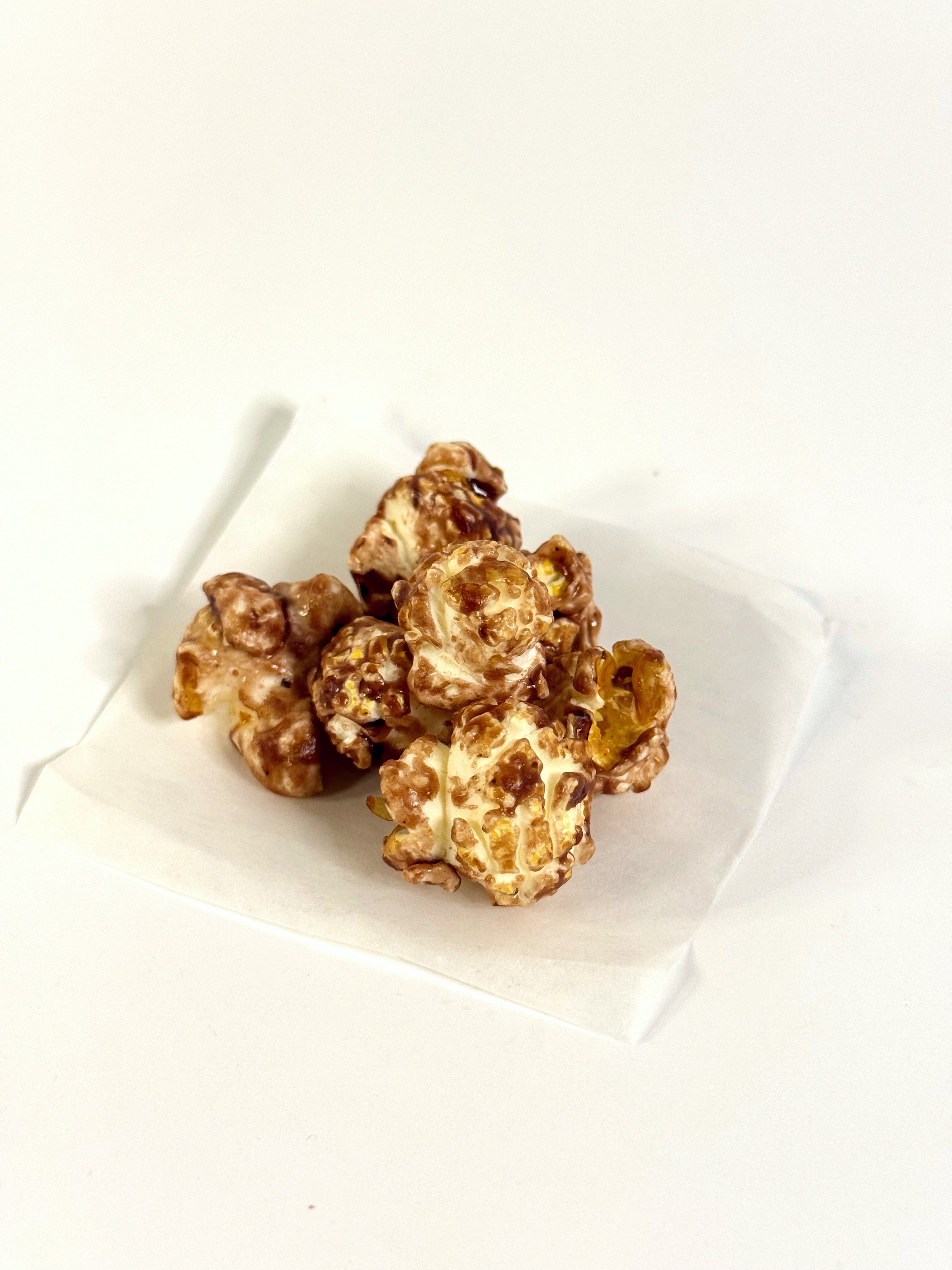 Caramel popcorn in a white paper bowl on a white background