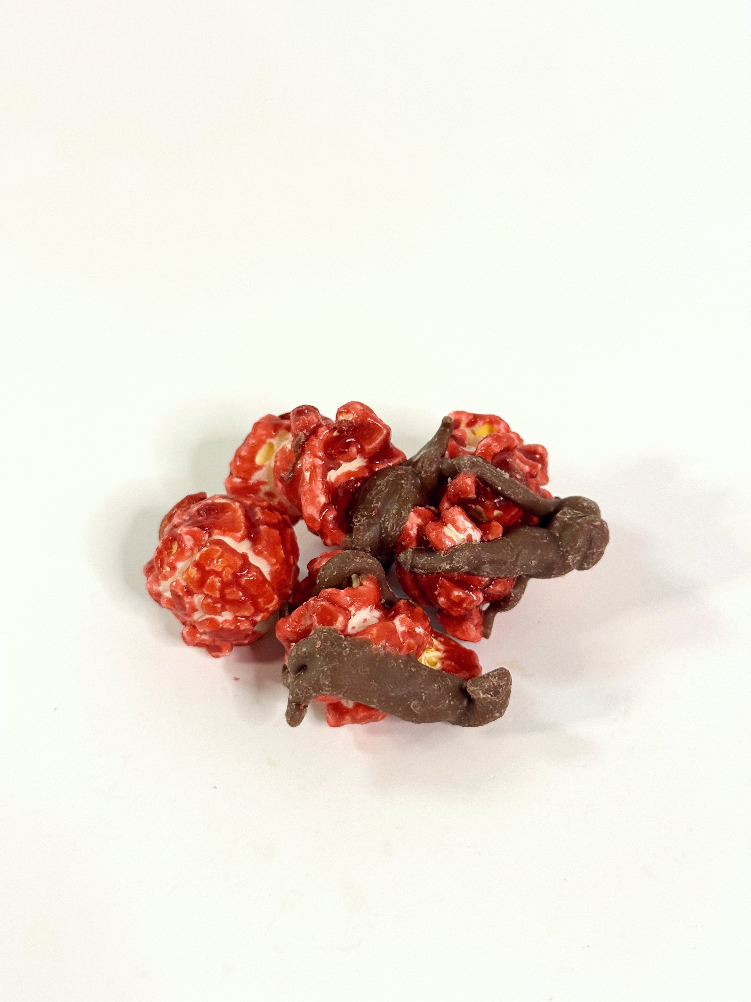 Red popcorn kernels with chocolate drizzle on a white background