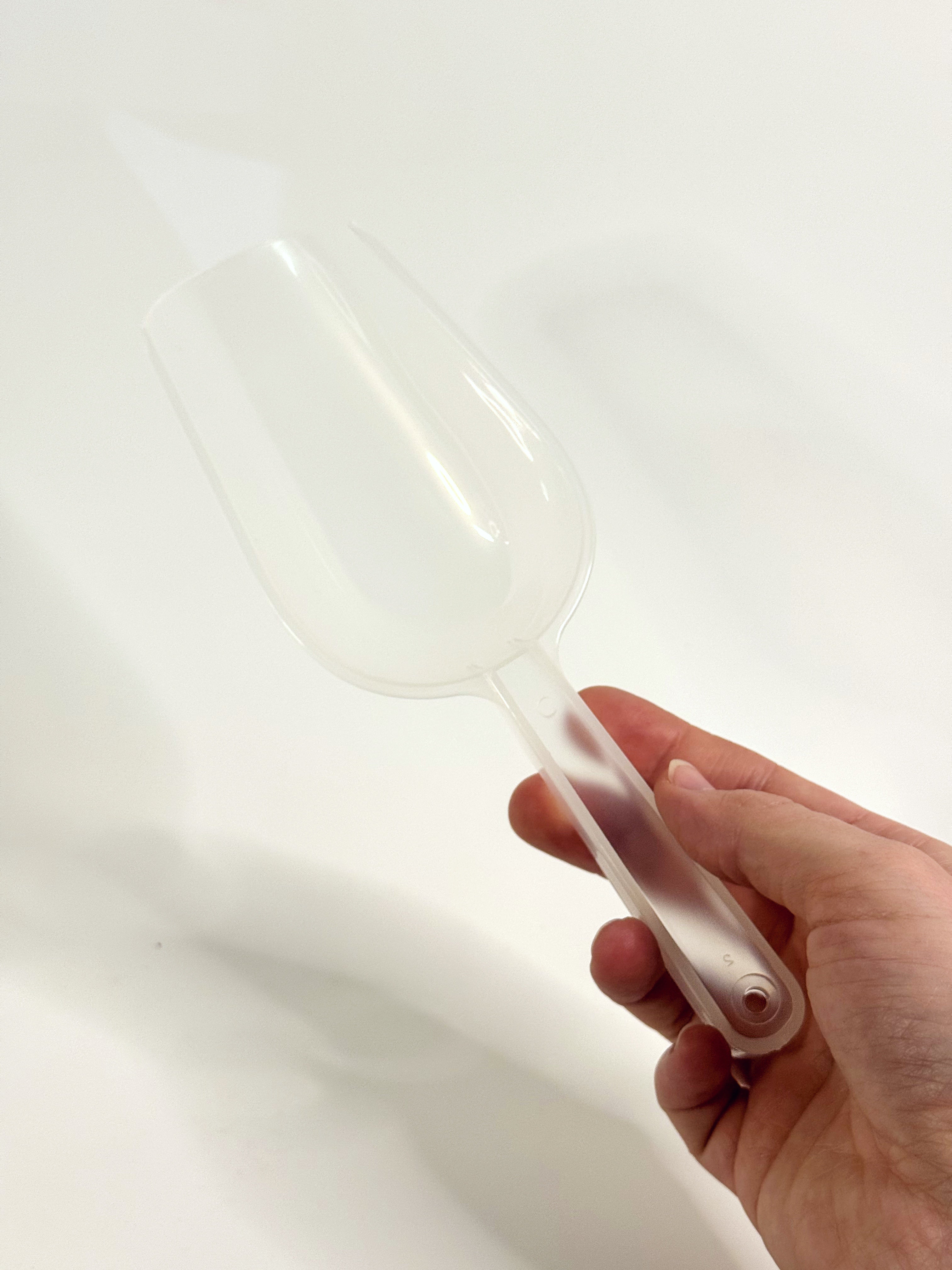 Clear plastic spatula held by a hand on a white background
