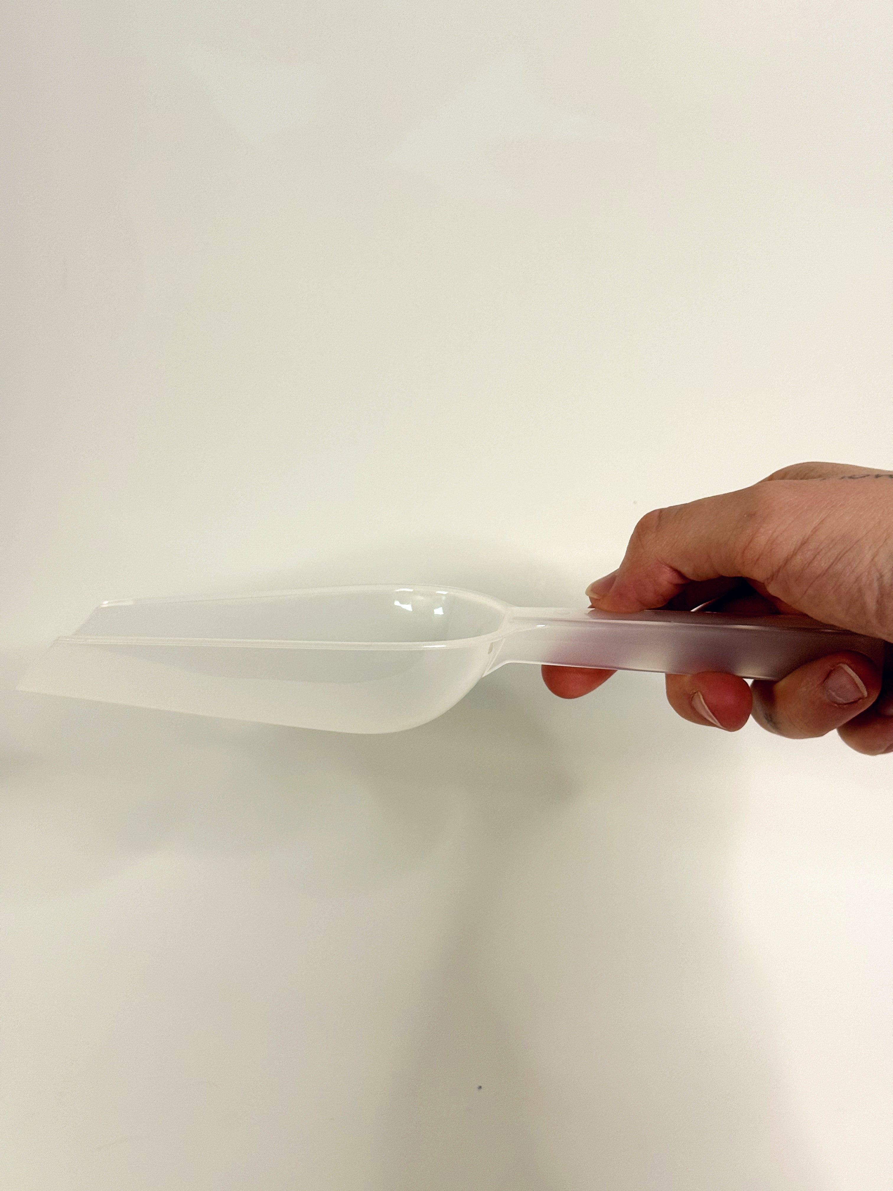 Hand holding a transparent plastic scoop against a white background