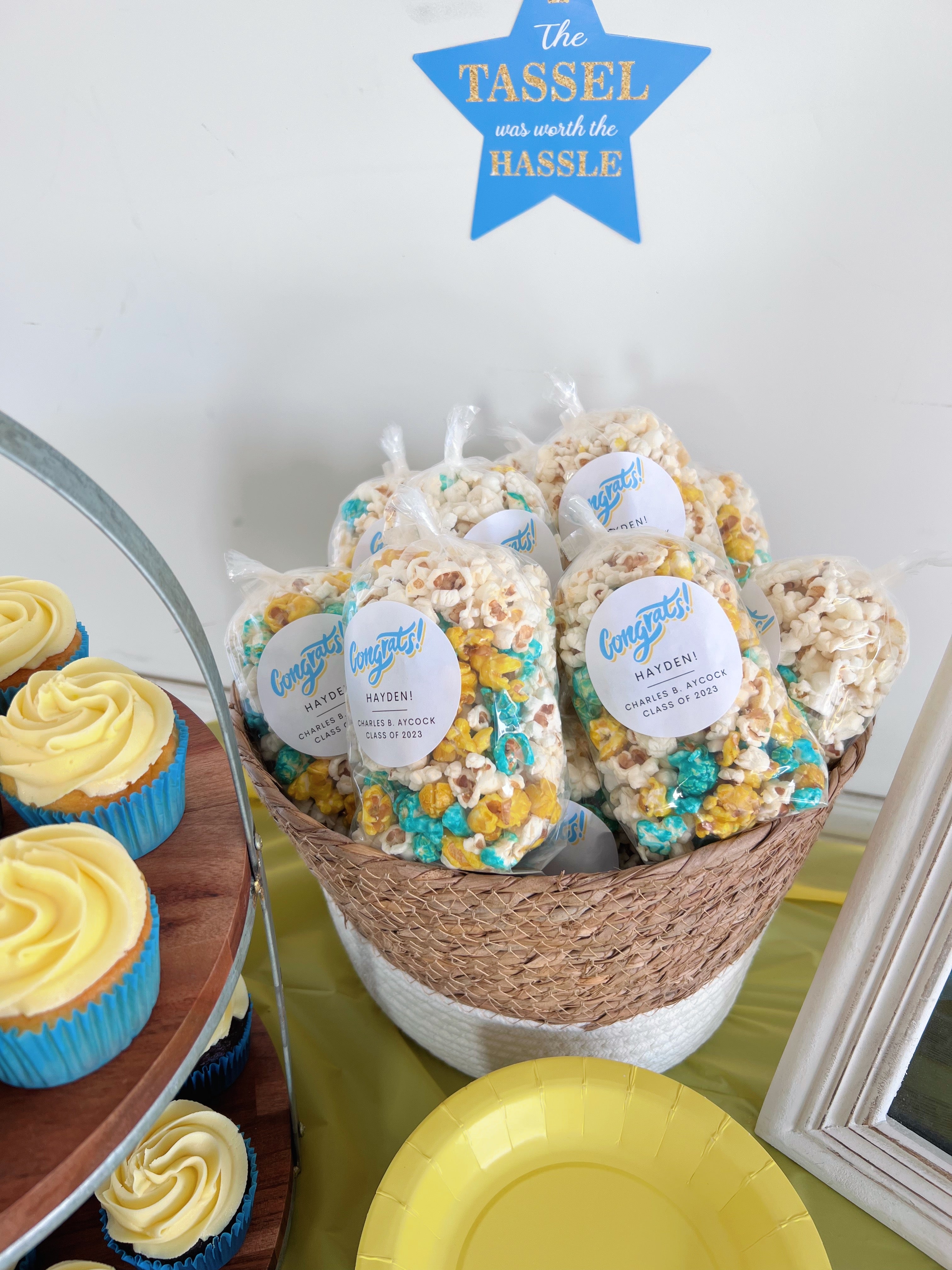 Basket of popcorn balls with labels on a table with cupcakes and plates. gourmet popcorn gift bag catering