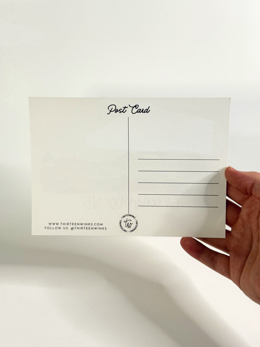 Hand holding a white postcard with text on a light gray background